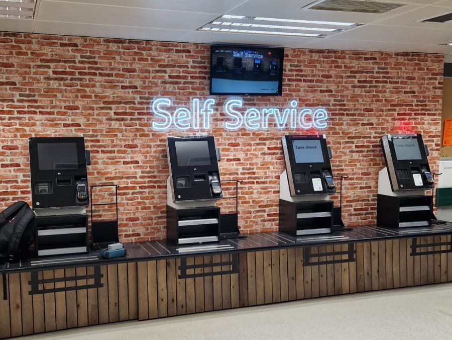 Pale blue LED signage on a brick wall background behind the self-service tills.