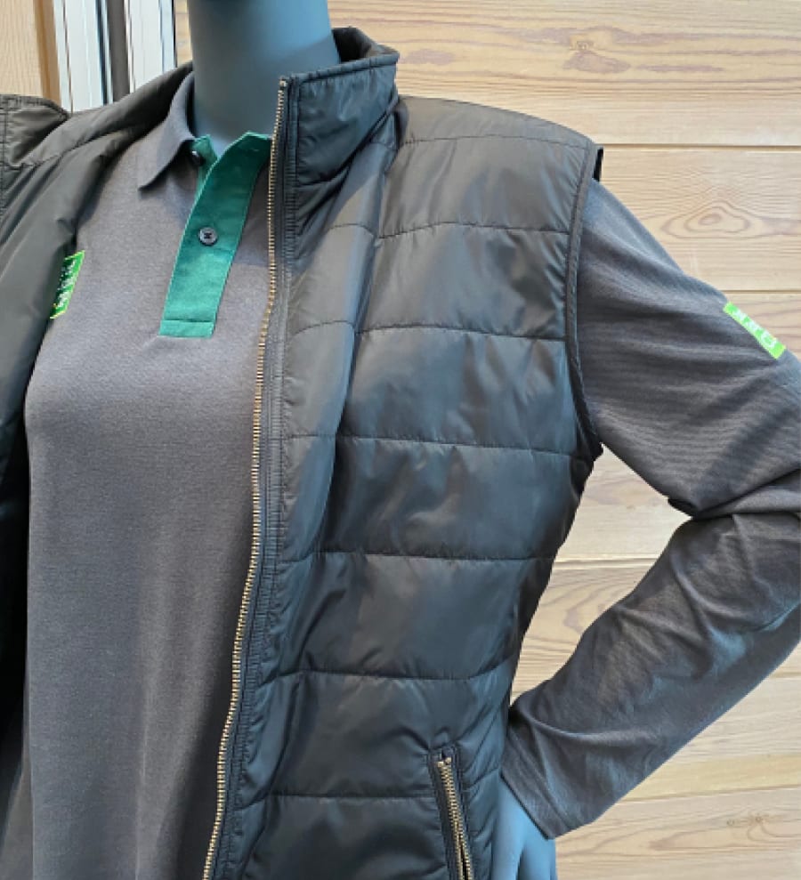 Sample uniform pieces: a dark grey long-sleeved polo shirt under a dark grey gilet, both have the company logo embroidered on.
