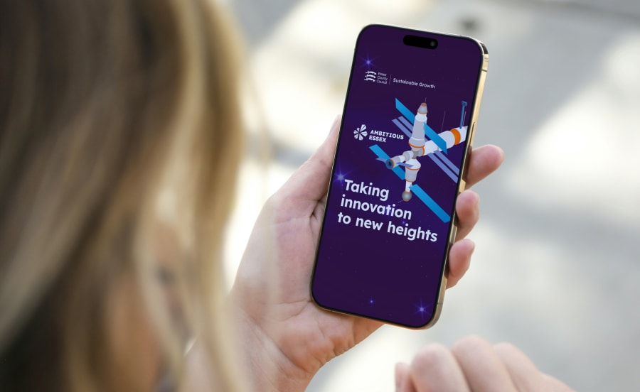 Close-up of someone viewing a post from the Ambitious Essex team on their phone, viewed over their shoulder as they hold it in their left hand.