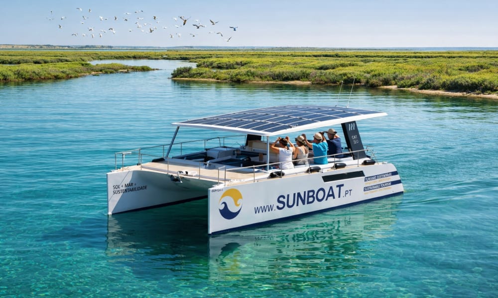 Um catamarã solar moderno e silencioso a deslizar pela lagoa cristalina da Ria Formosa no Algarve.