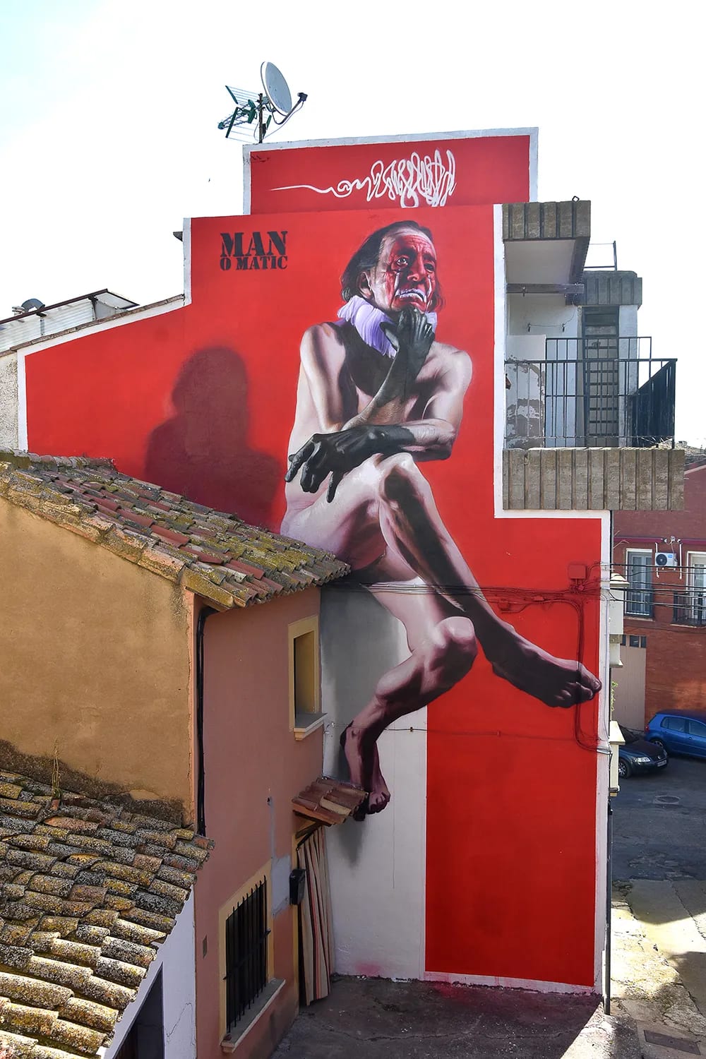Mural de un hombre desnudo con la cara roja y negra en una pared roja.