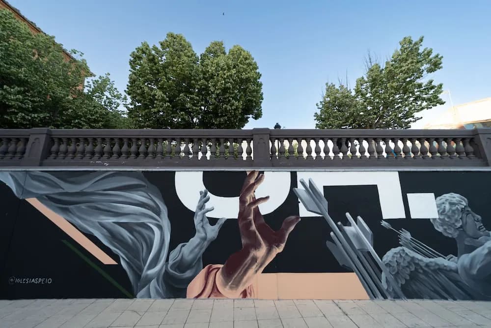 Mural con figuras grises y una mano roja alcanzando algo, bajo un puente.