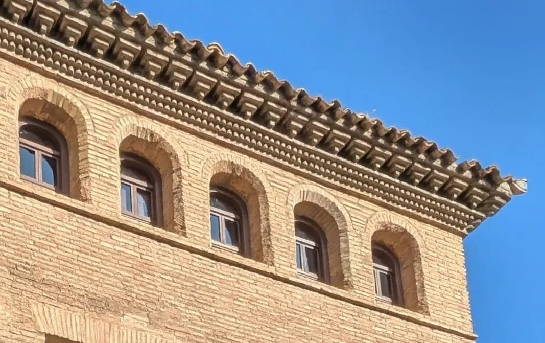 Fachada de edificio antiguo con cinco ventanas arqueadas y tejado de tejas bajo cielo azul.