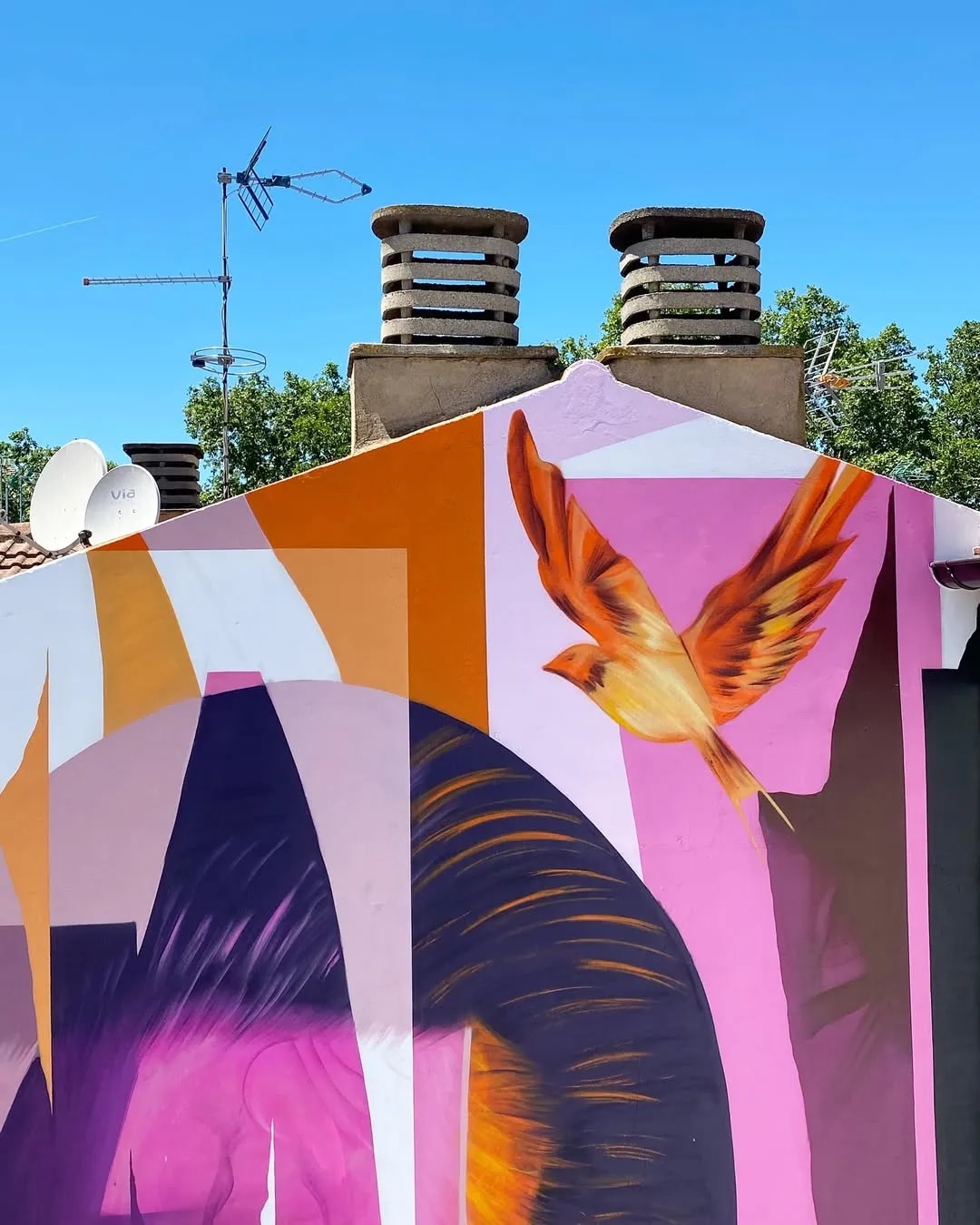 Mural colorido con un pájaro naranja volando sobre un fondo rosa y púrpura.