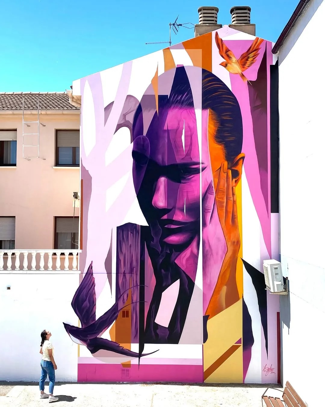 Mural de una mujer con tonos rosados y morados en una pared urbana.