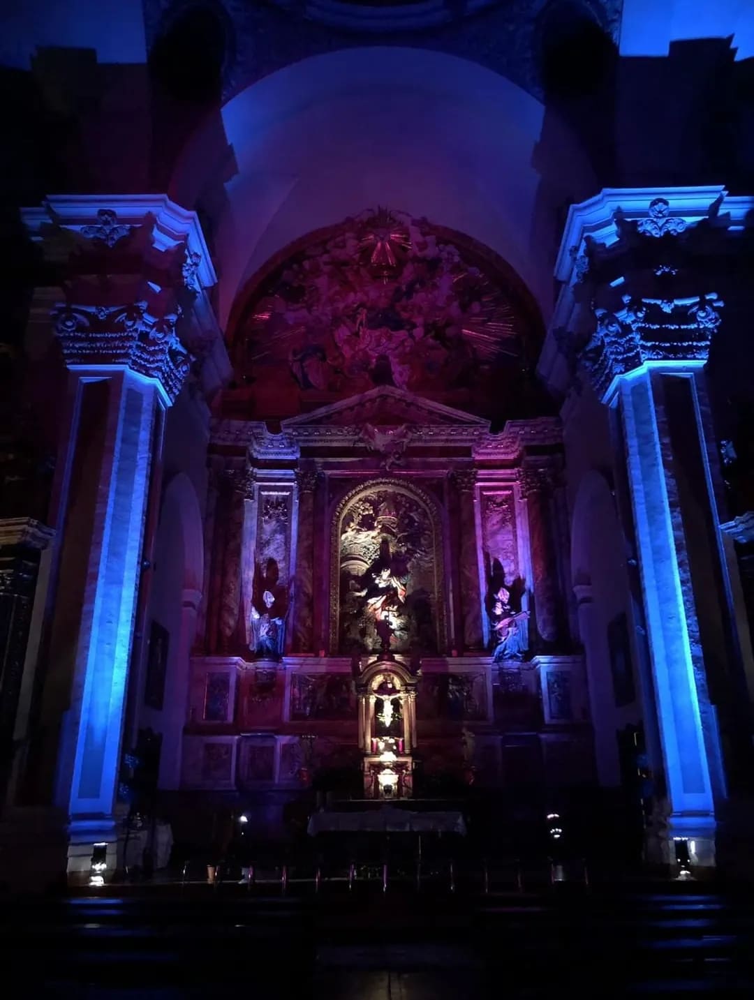 Interior de una iglesia con altar y columnas iluminadas con luz azul y roja.
