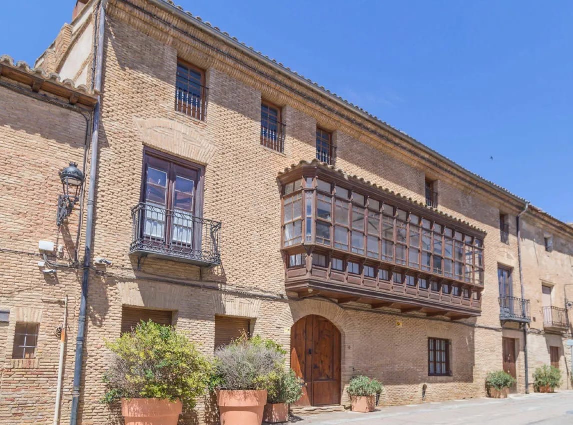 Casa antigua de ladrillo con balcones de madera y macetas en la entrada