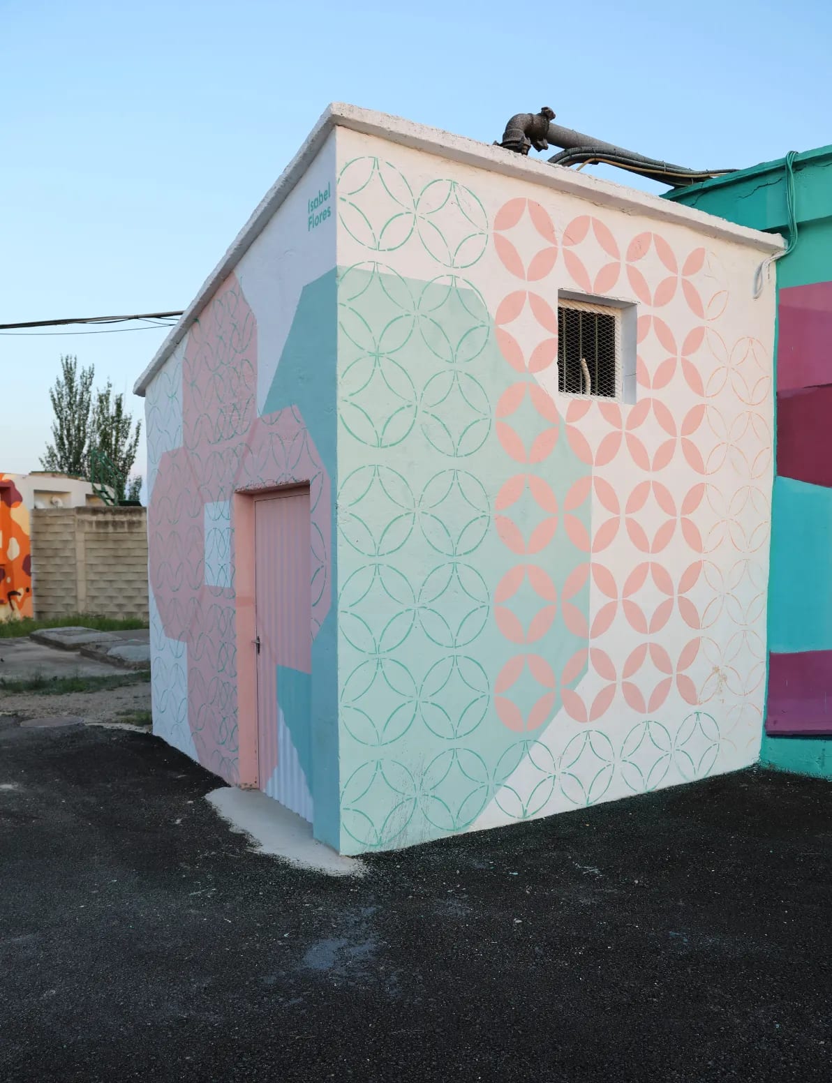 Un pequeño edificio con una puerta rosa y un patrón de flores pintado en la pared lateral.