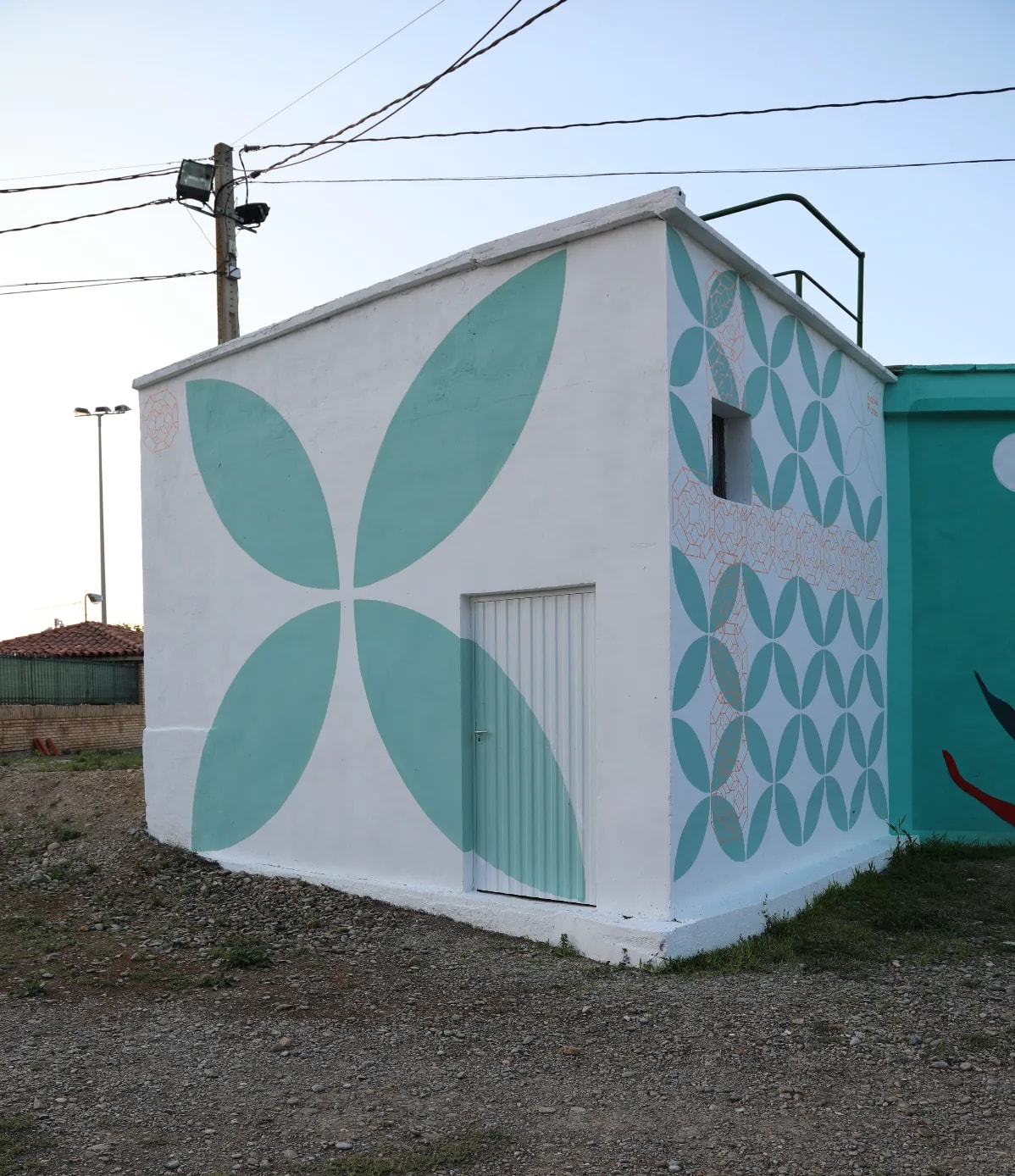 Un pequeño edificio blanco con un diseño de flor de cuatro pétalos en tonos azulados y una puerta azul.