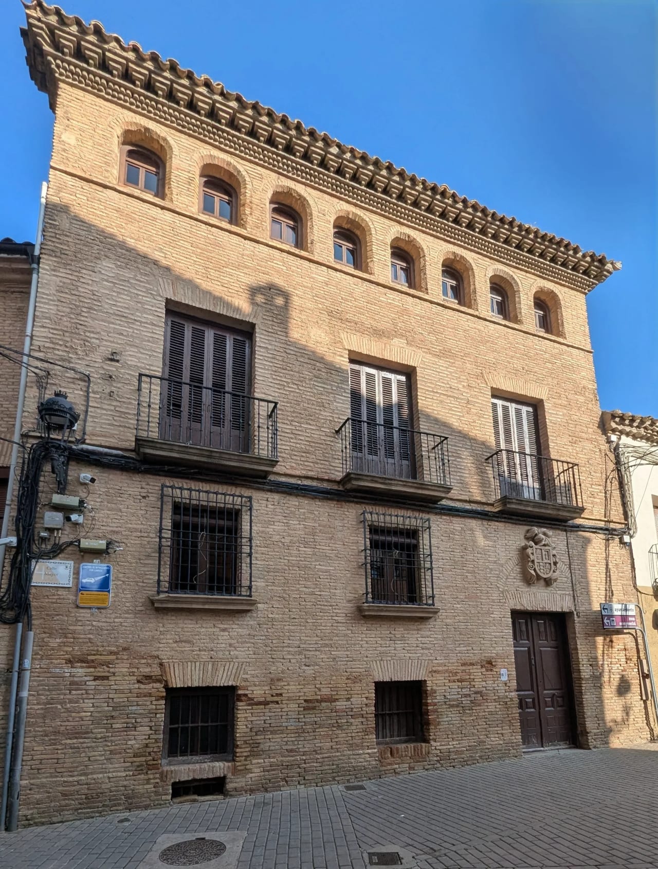 Edificio de tres pisos con fachada de ladrillo claro, balcones y puerta principal de madera oscura.