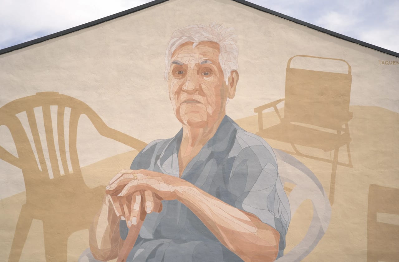 Mural de un hombre mayor con sillas en el fondo en una pared beige.