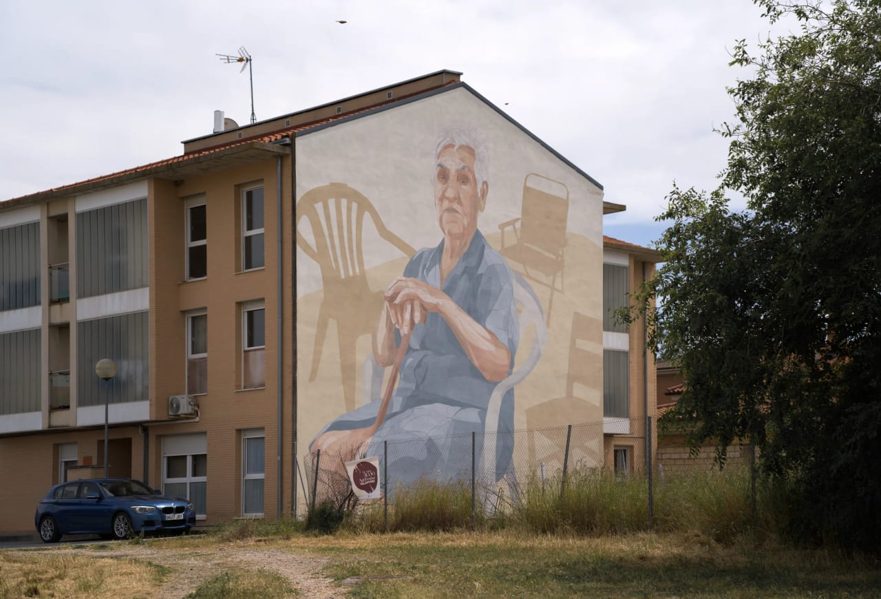 Un mural en un edificio que muestra a un anciano sentado en una silla.