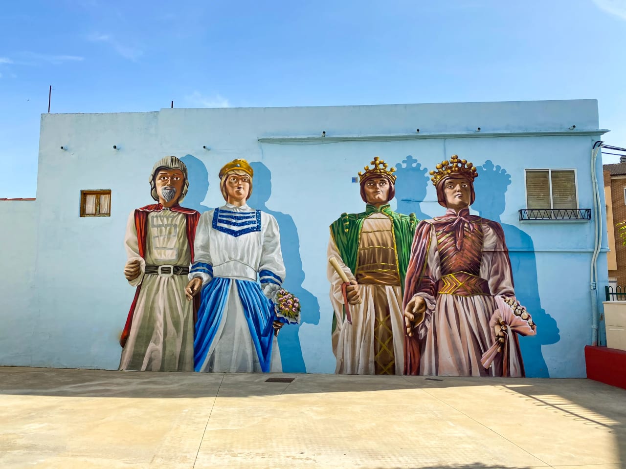Cuatro figuras históricas pintadas en una pared azul claro, vestidas con ropa tradicional.