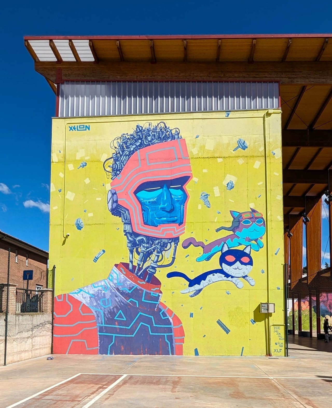 Mural colorido de una persona con máscara futurista y gatos robóticos en una cancha de baloncesto.