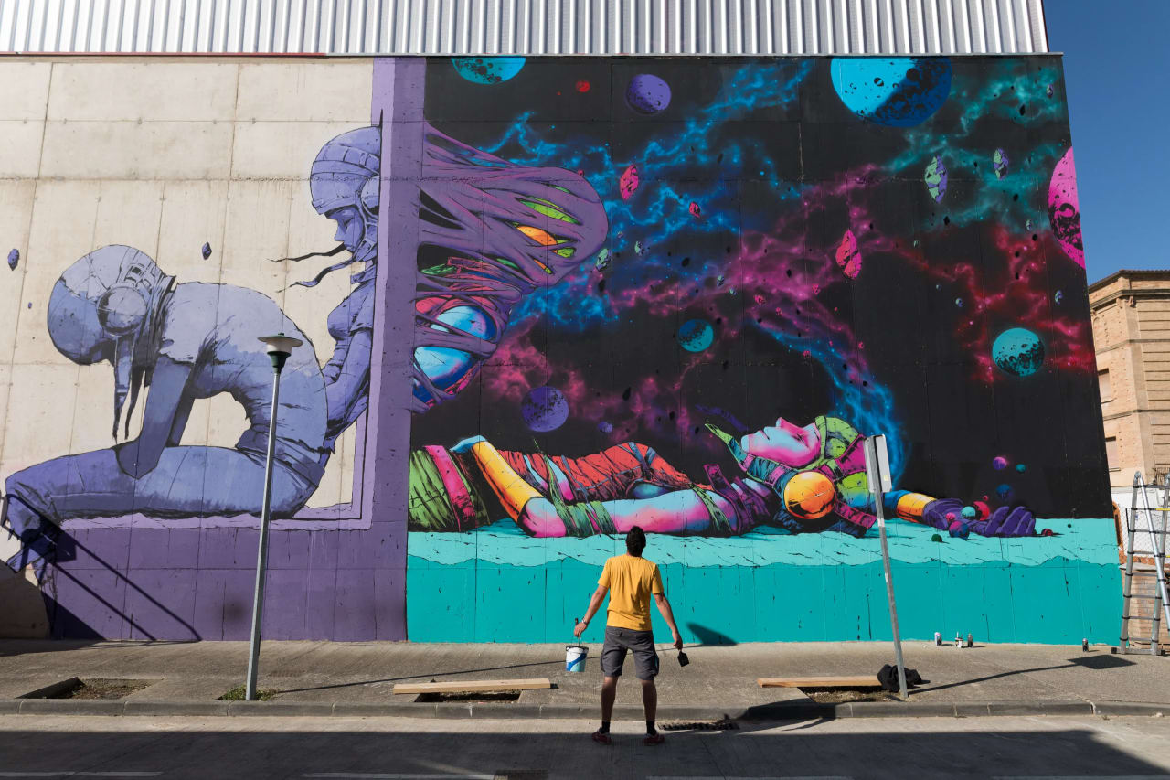 Un hombre pinta un mural colorido en una pared exterior.