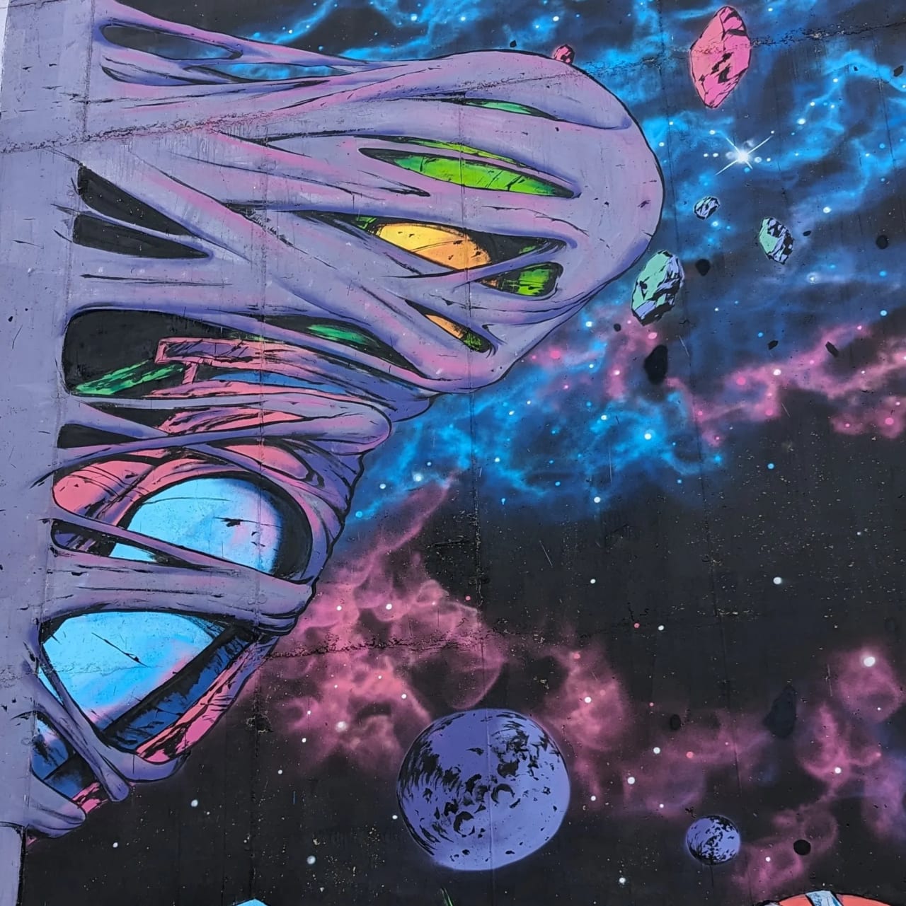 Mural de un alienígena en el espacio con planetas y nebulosas.