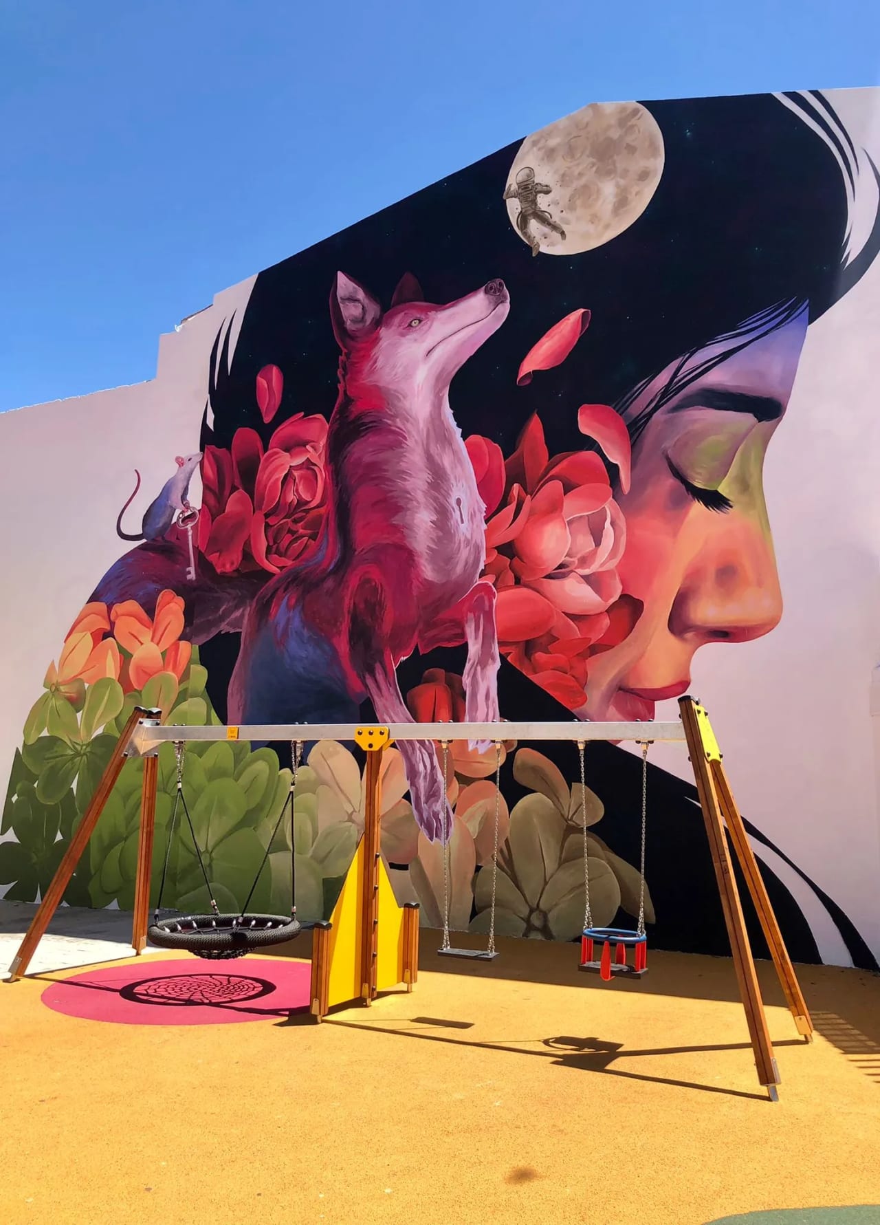 Mural de una mujer con flores y un lobo, con columpios delante.
