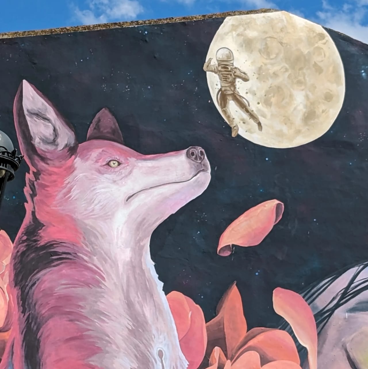 Un mural con un zorro rosa que mira a un astronauta saltando en la luna llena.