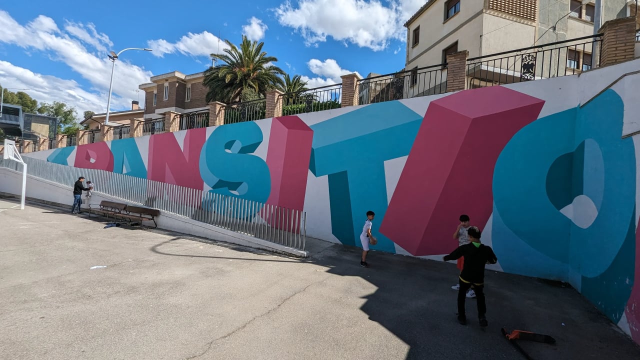 Niños jugando frente a un mural con la palabra "TRANSITIO" en una pared.