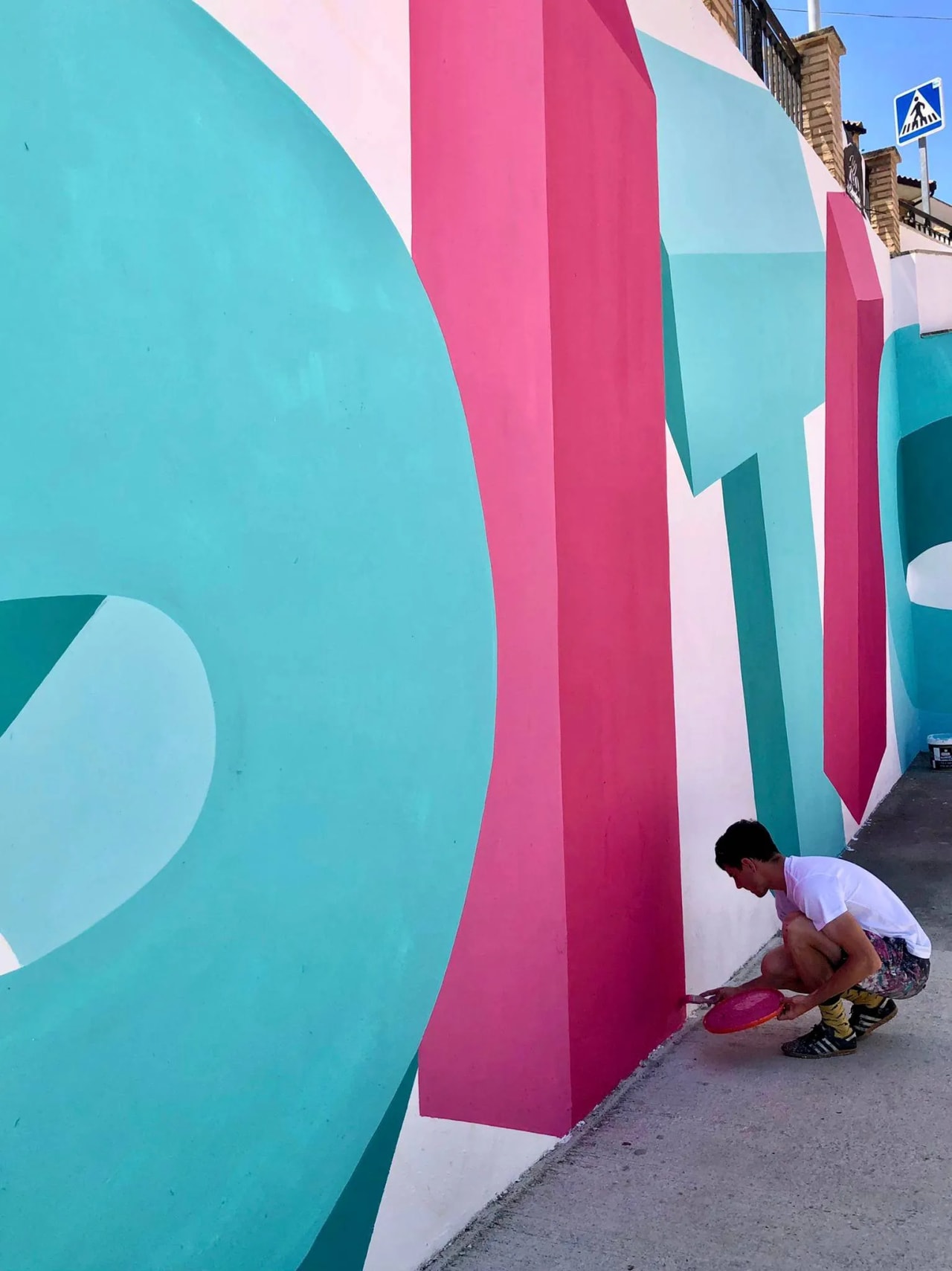 Hombre pinta un mural colorido en una pared con un plato de pintura.