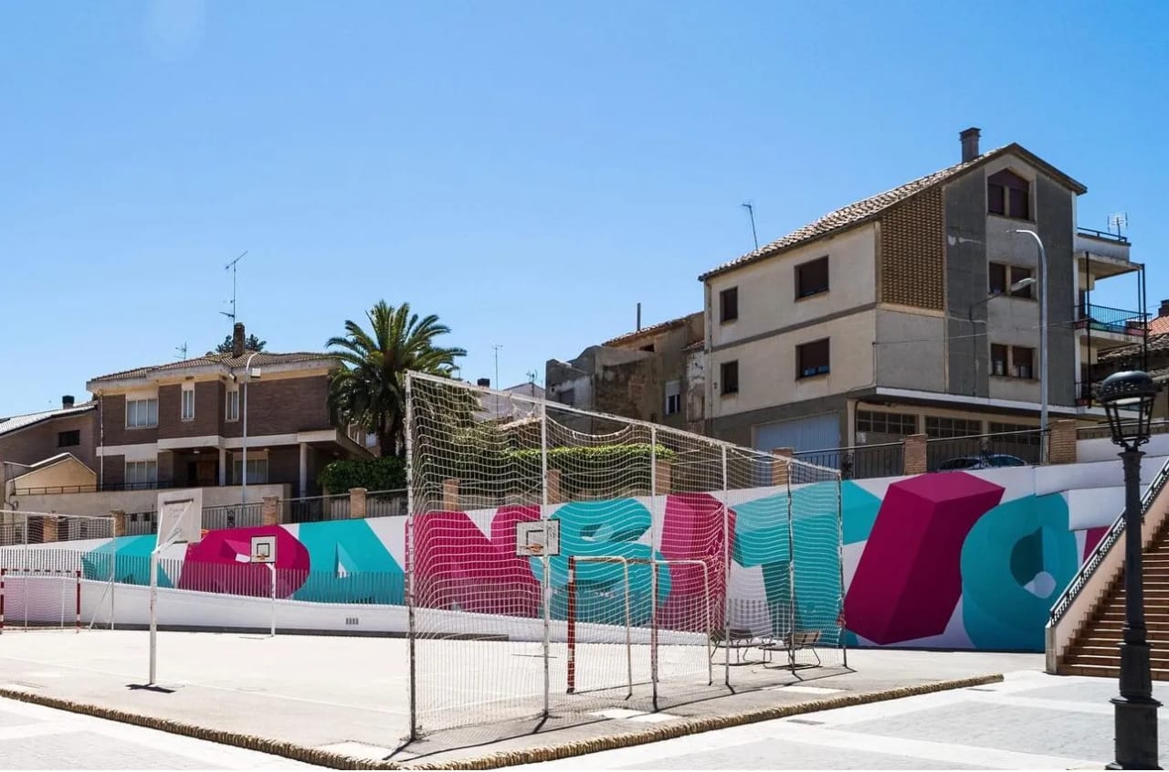 Cancha de baloncesto con muro decorado en colores magenta y celeste.