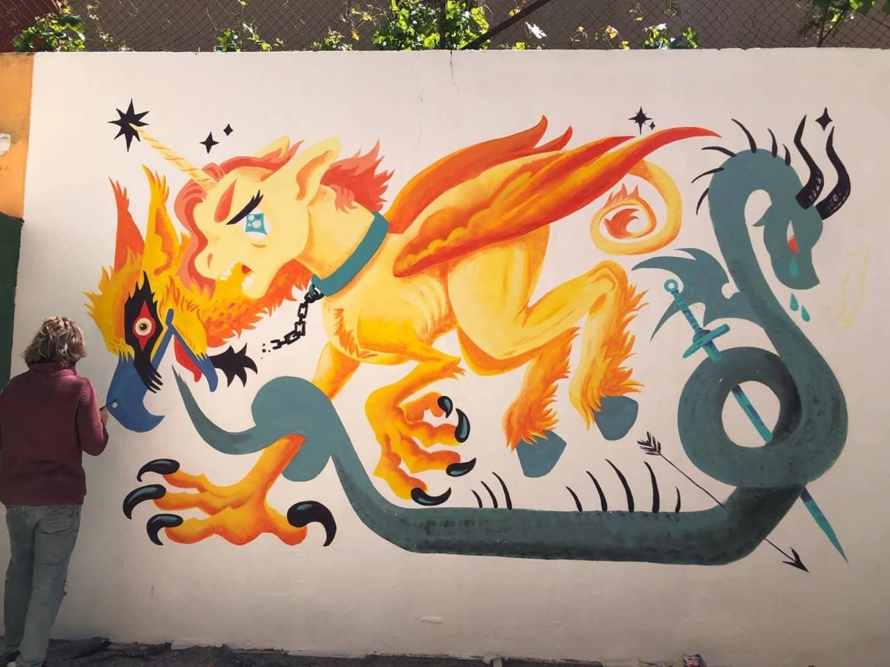 Mural de un dragón o león con cola de serpiente en colores naranjas, amarillos y verdes.