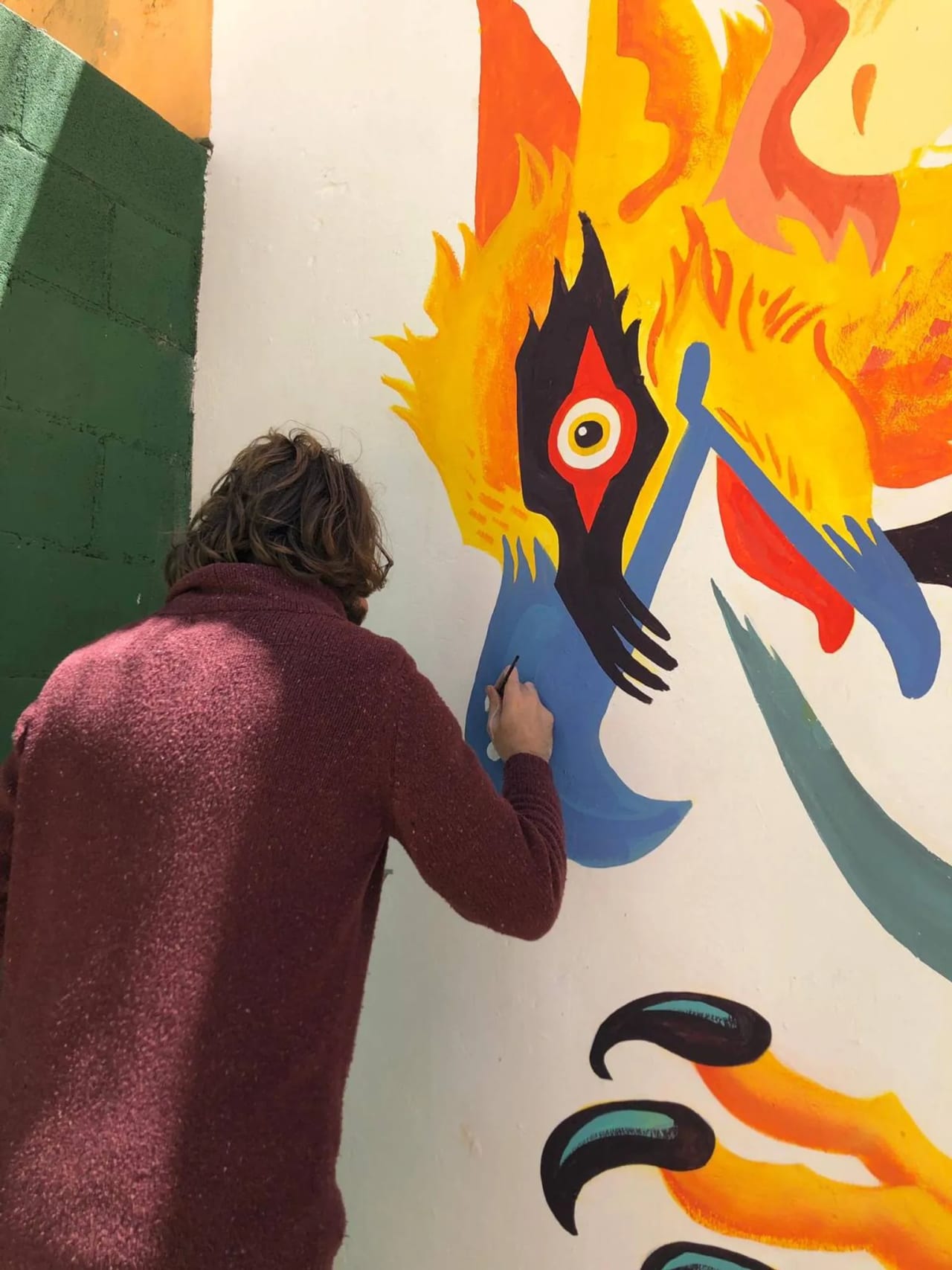 Persona pintando un mural abstracto en una pared blanca con colores brillantes.