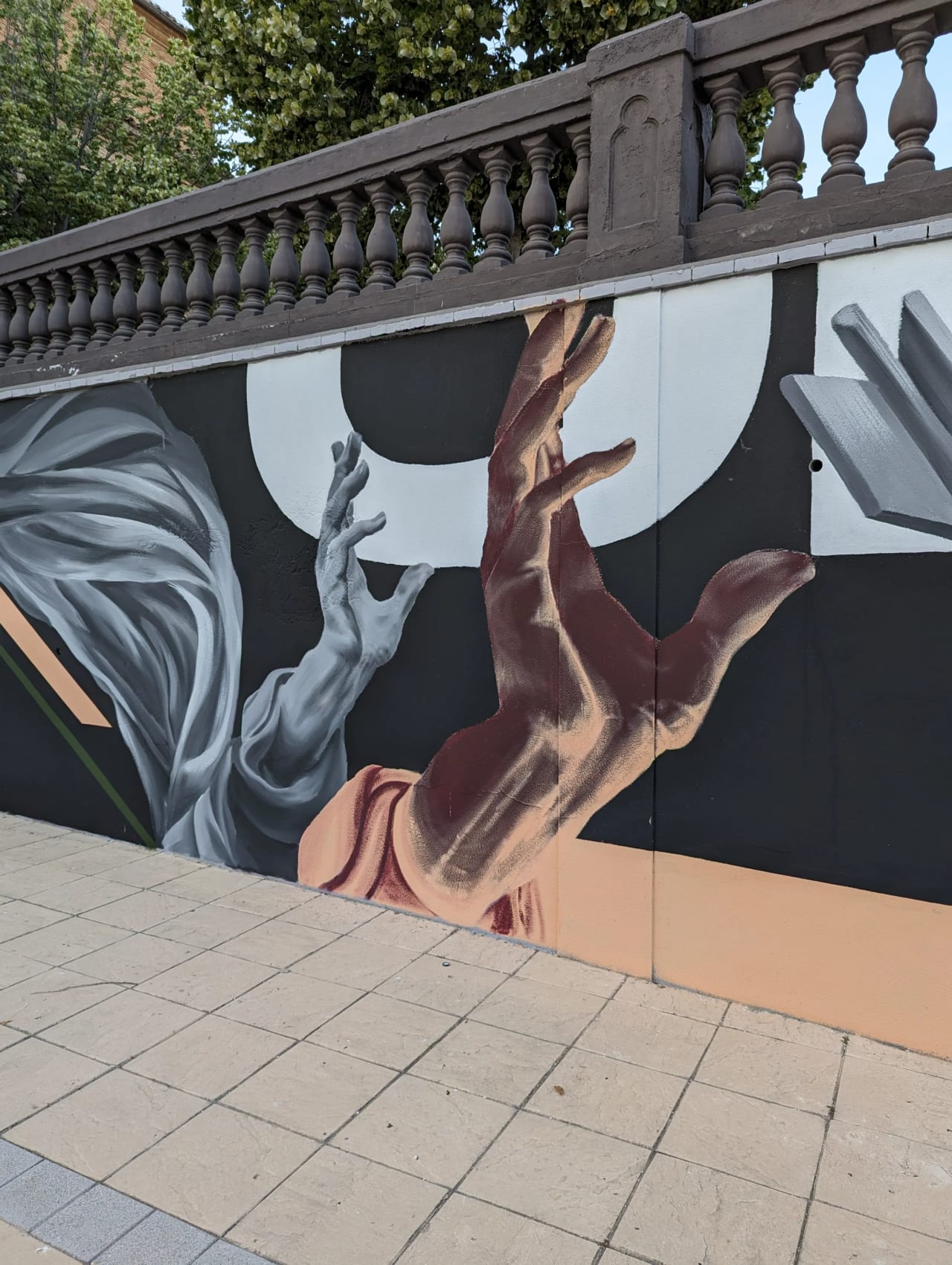 Mural con manos extendidas hacia arriba en colores grises y marrones sobre fondo negro.