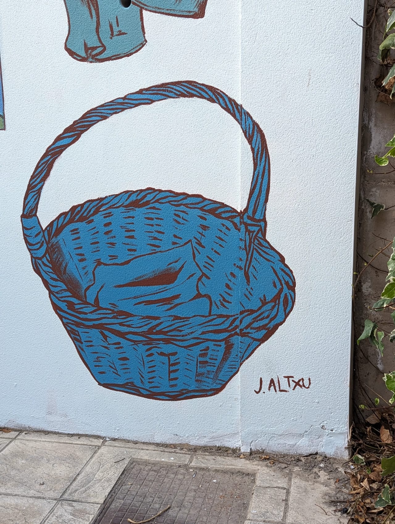 Cesta azul con mango, dibujada en pared blanca con técnica de pintura.