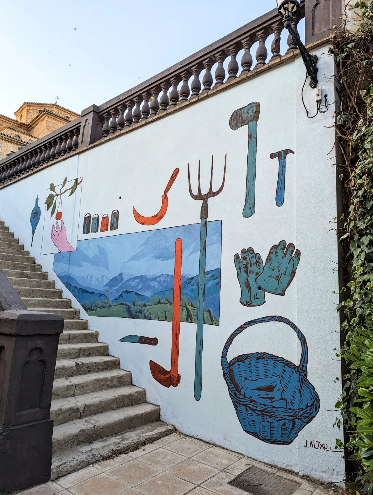 Mural en una pared blanca con herramientas y un paisaje montañoso.