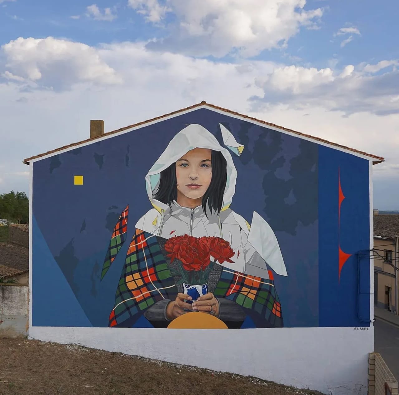 Mural de una joven con flores en un edificio bajo un cielo nublado.