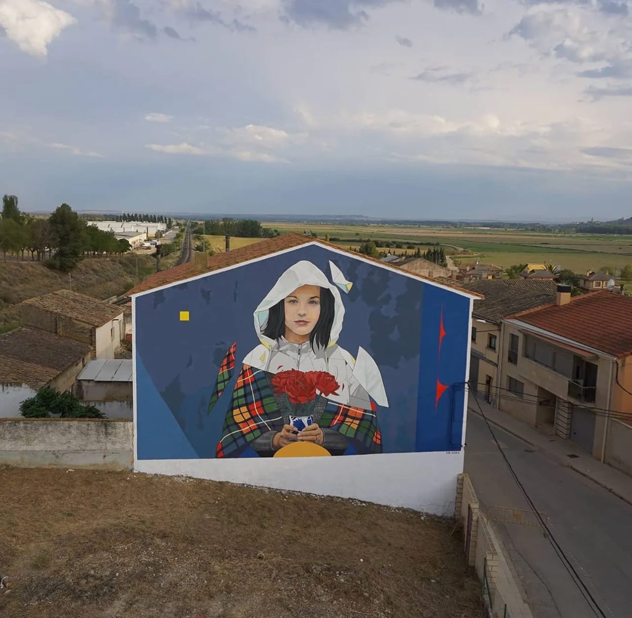 Mural de una chica con capucha sosteniendo rosas rojas en una pared azul.