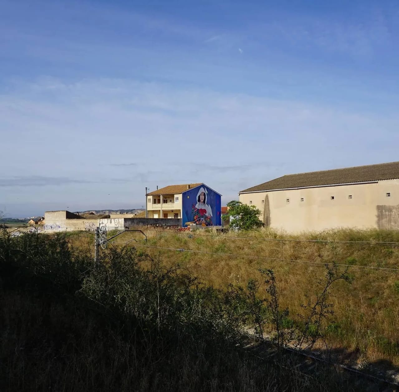 Mural de una niña en un edificio azul en un paisaje rural.