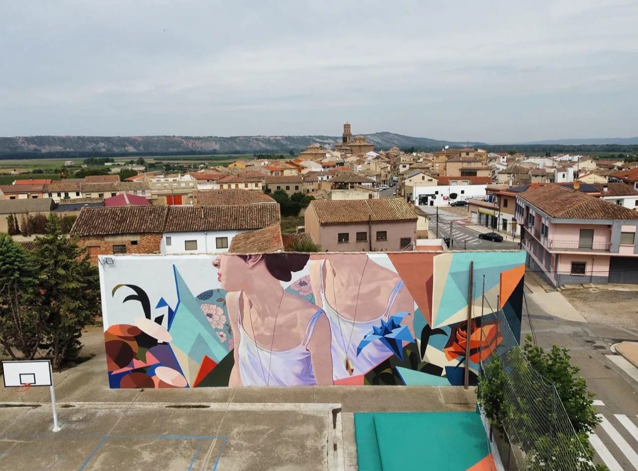 Mural de una mujer con fondo geométrico y floral en un barrio.