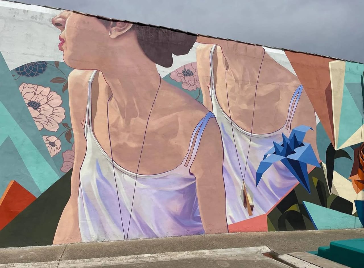 Mural de una mujer con vestido blanco y fondo geométrico colorido.
