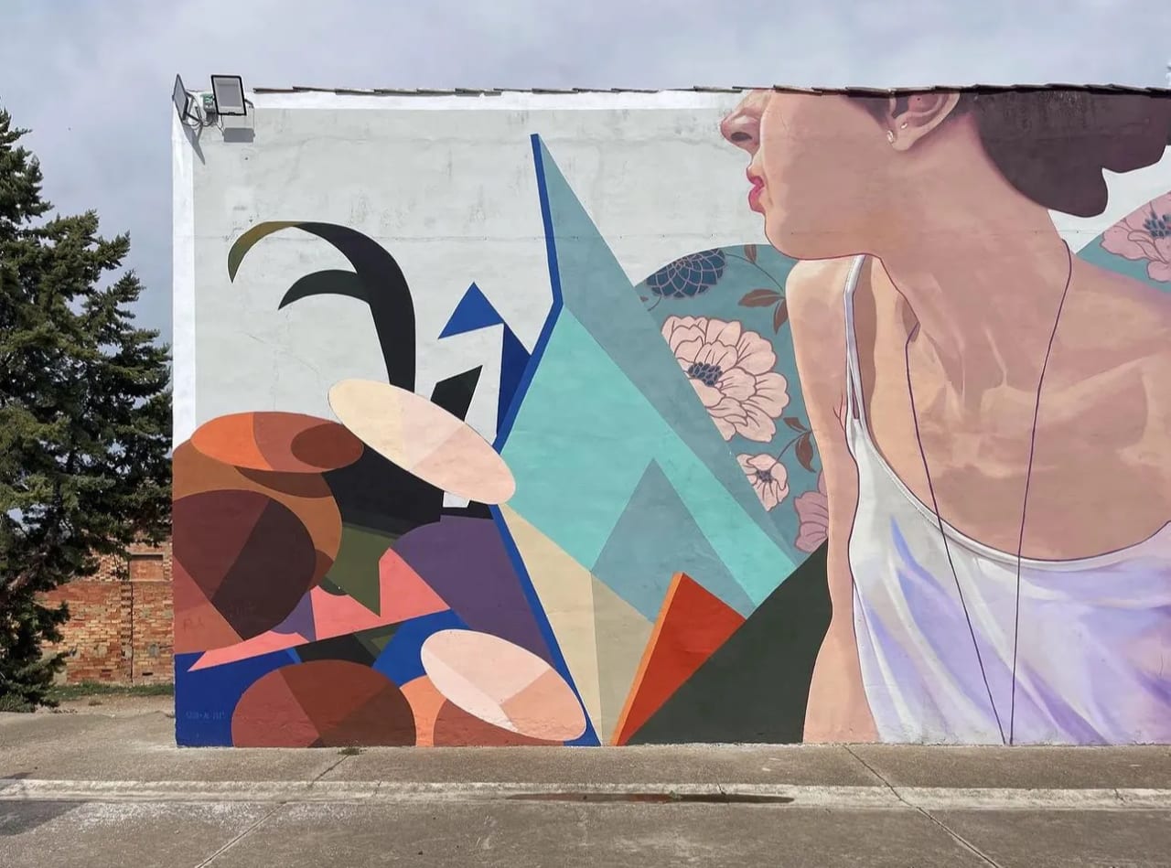 Mural de una mujer con vestido blanco y flores en el fondo.