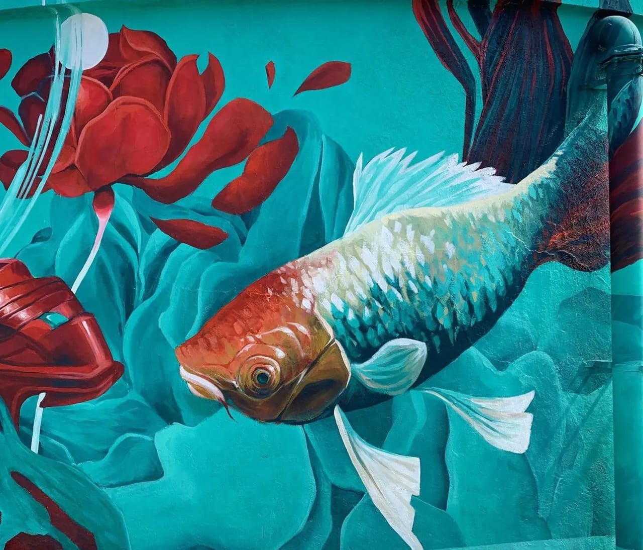 Pez dorado nadando entre una flor roja y algas en un mural colorido.