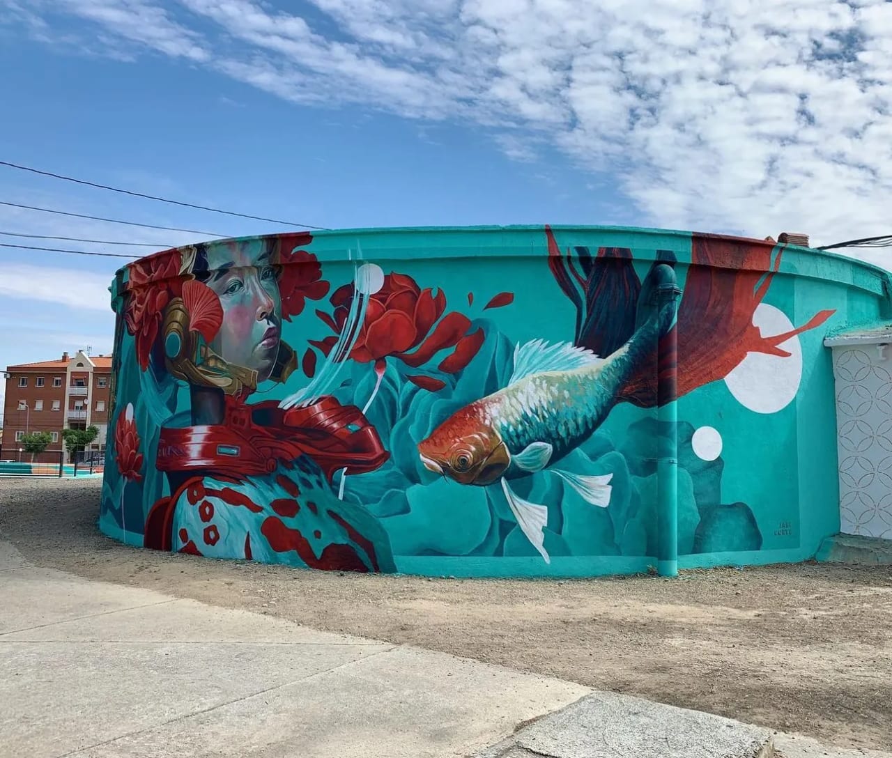 Mural de un pez y una mujer en una pared cilíndrica azul turquesa.