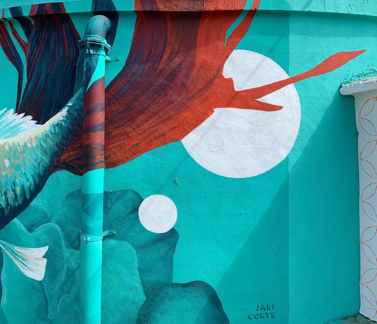 Mural de colores en una pared con un pájaro rojo y un fondo azul turquesa.