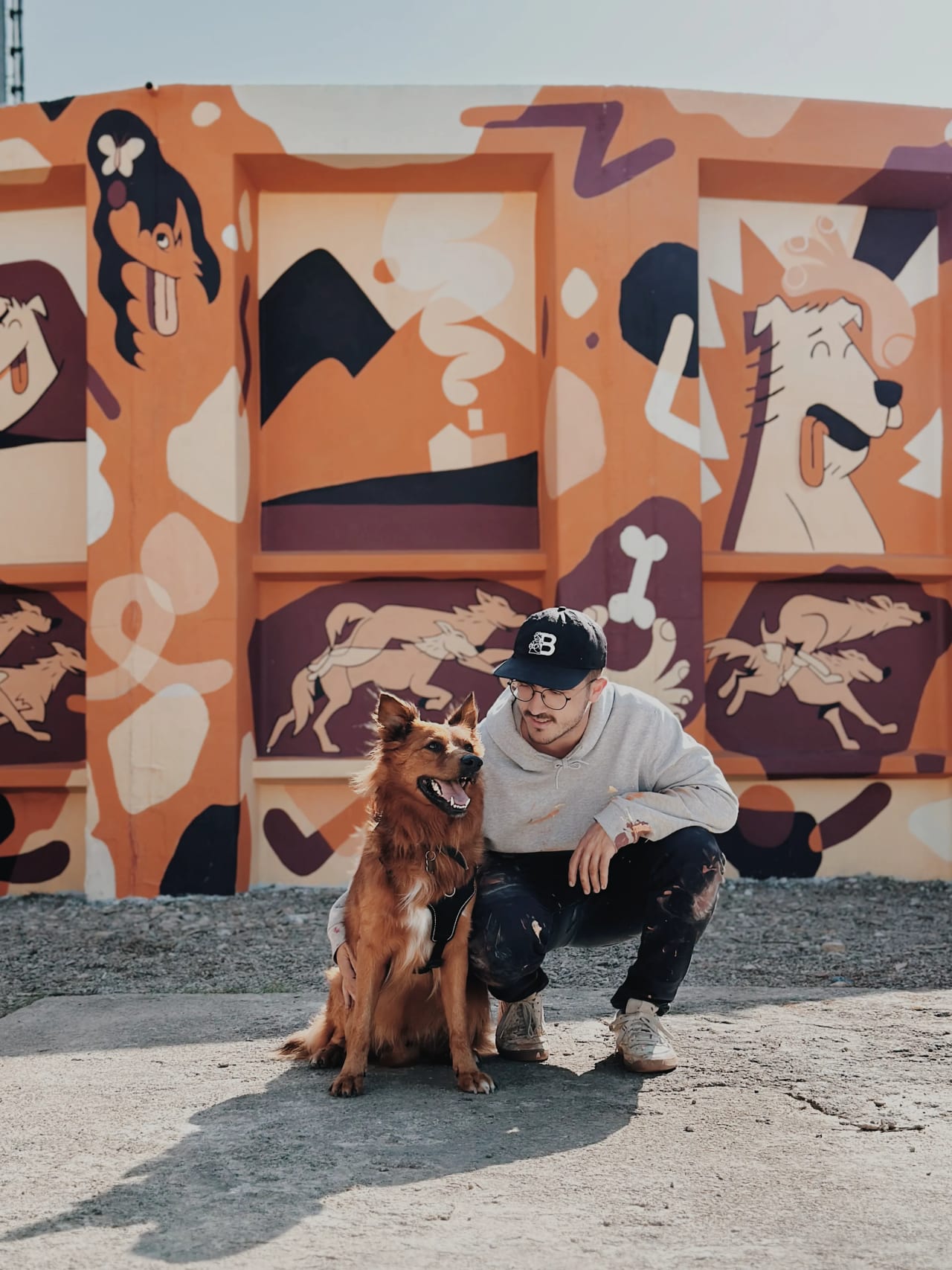 Un hombre y su perro frente a un mural colorido.