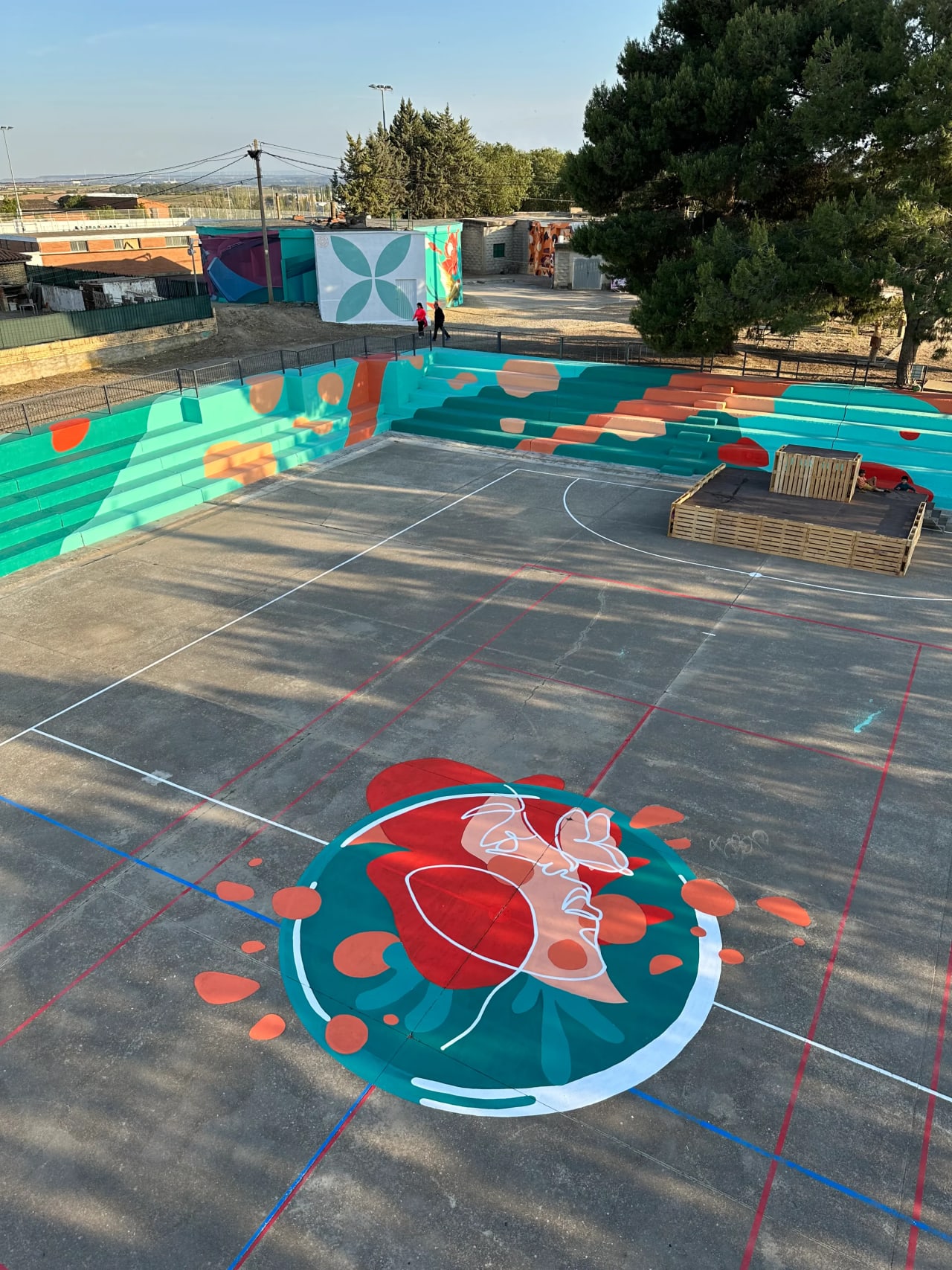Pista de baloncesto con diseño mural colorido en el suelo y gradas.