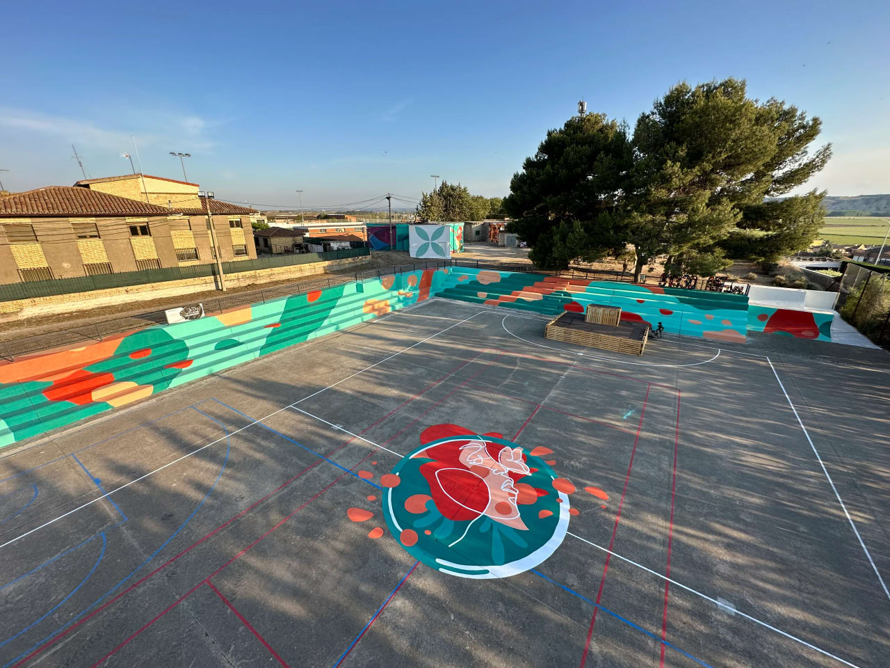 Pista de baloncesto con grafitis coloridos y árboles al fondo.