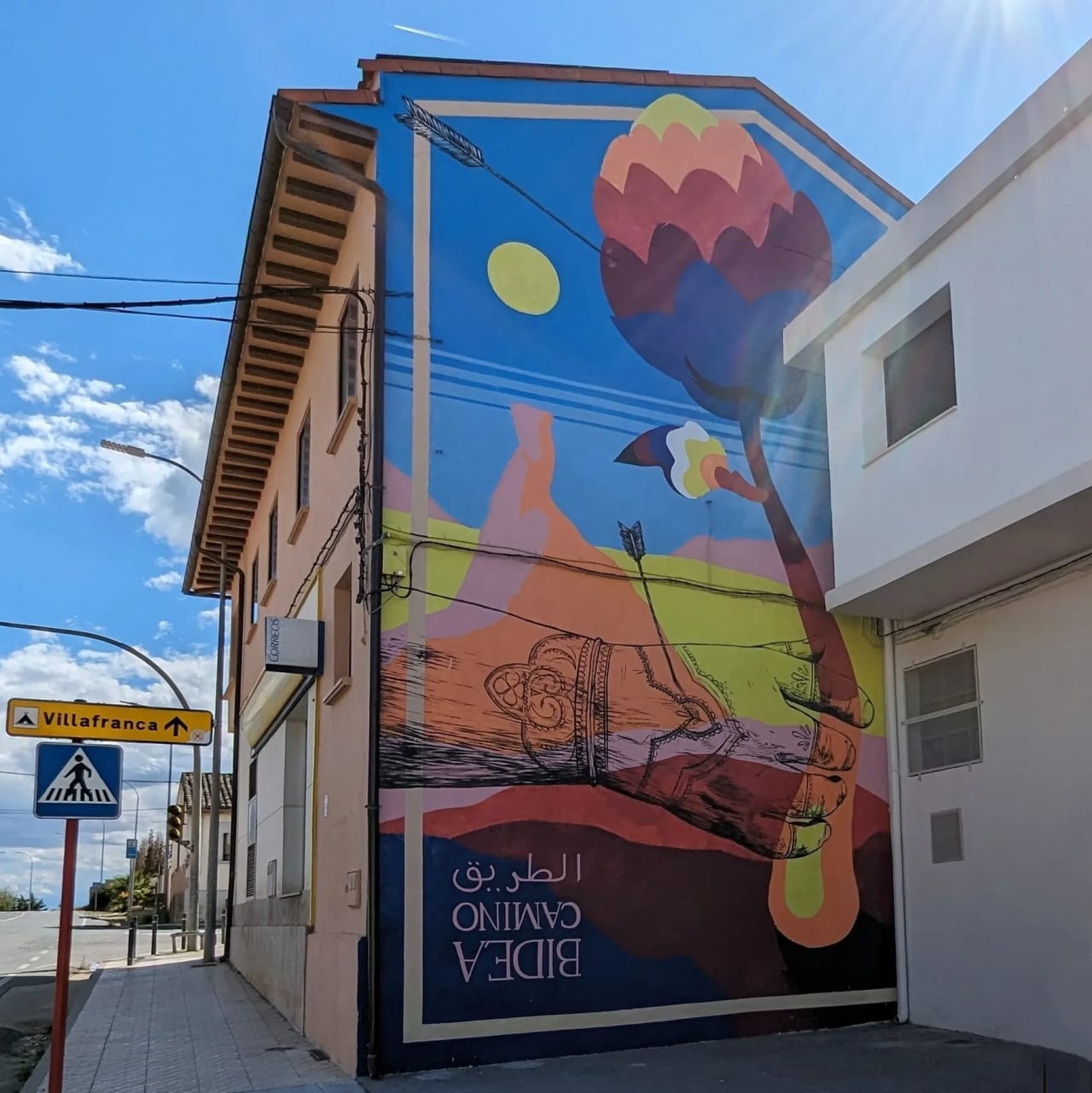 Mural en una pared de un edificio con un paisaje colorido y una mano tatuada.