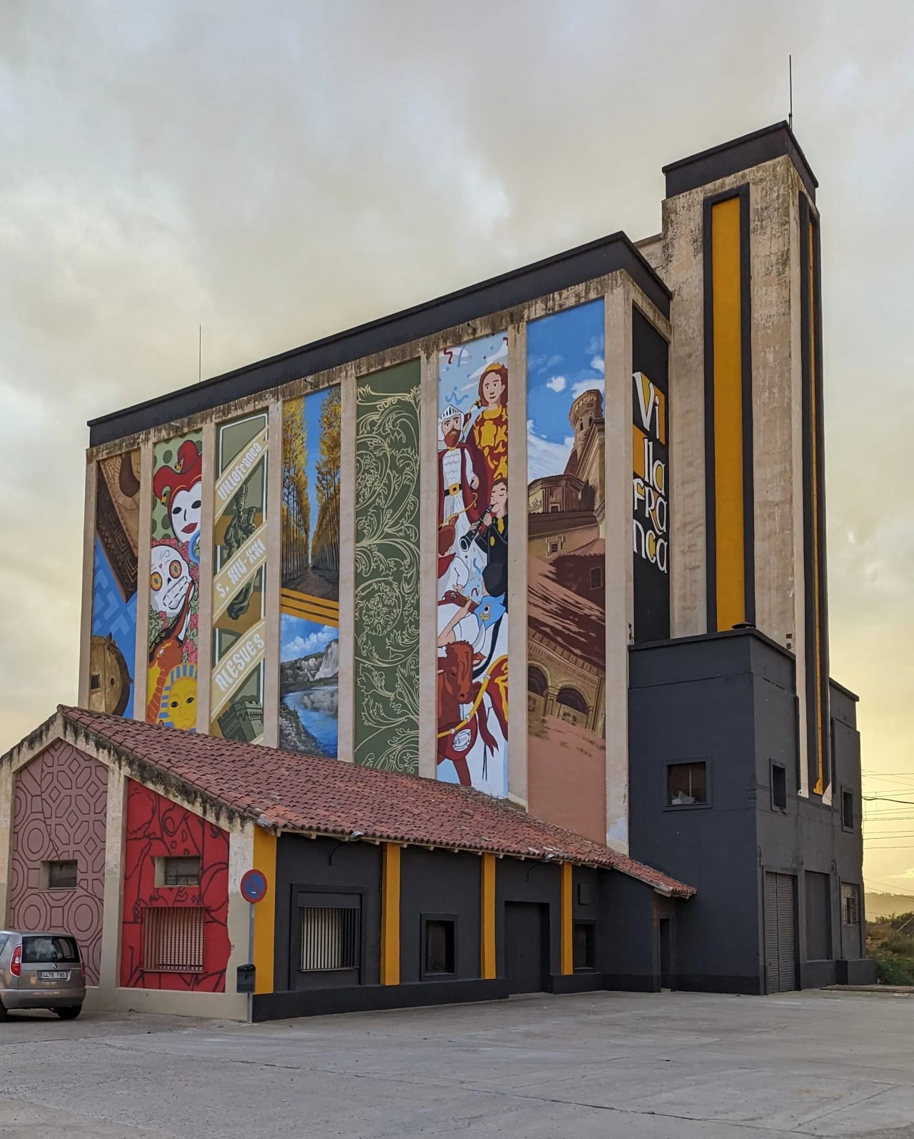 Un gran edificio con un mural colorido en la fachada, mostrando diversas escenas y figuras.