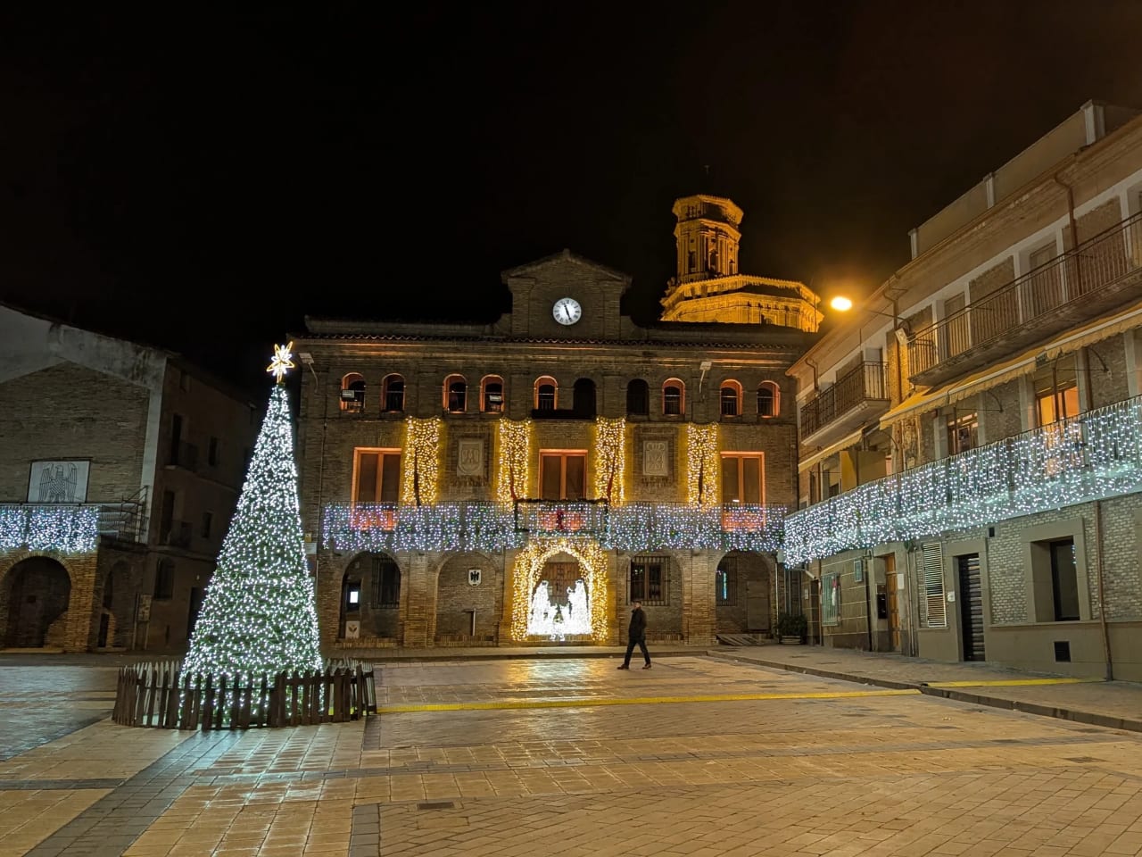 Árbol de Navidad iluminado en una plaza con edificios decorados en una ciudad.