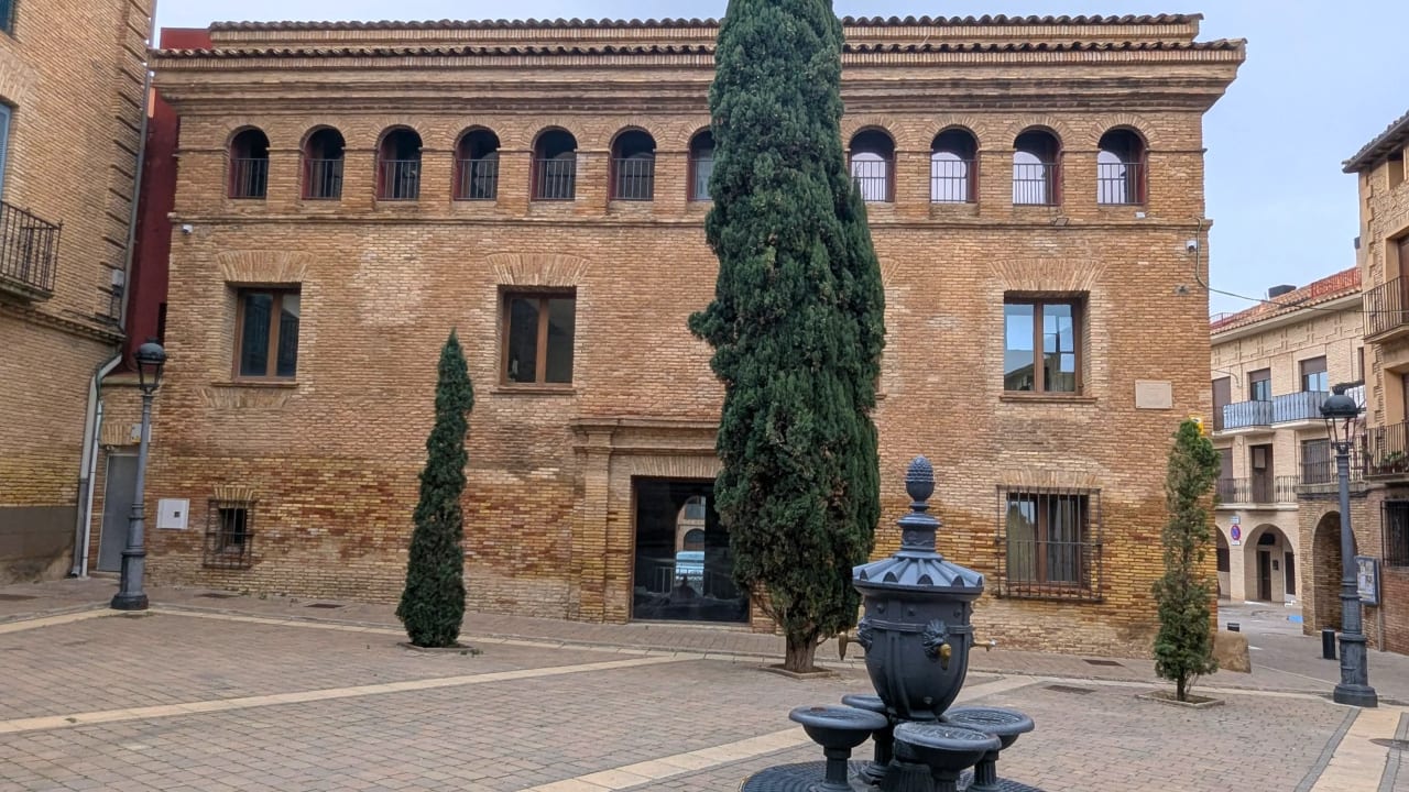 Un edificio histórico de ladrillos con ventanas arqueadas y un patio tranquilo con fuente y árboles.