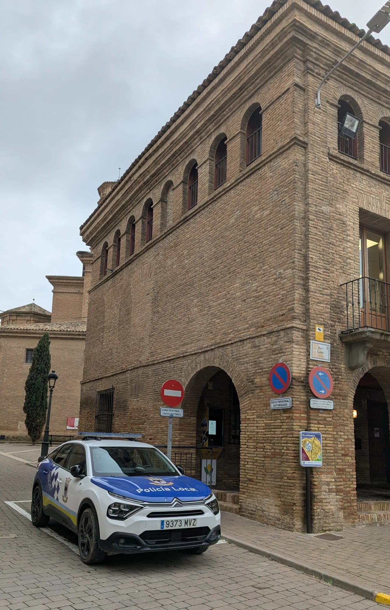 Vehículo de la Policía Local en una calle empedrada junto a un edificio histórico.
