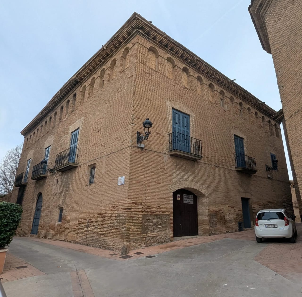 Edificio histórico de ladrillo visto desde la esquina, con balcones y puertas de madera.