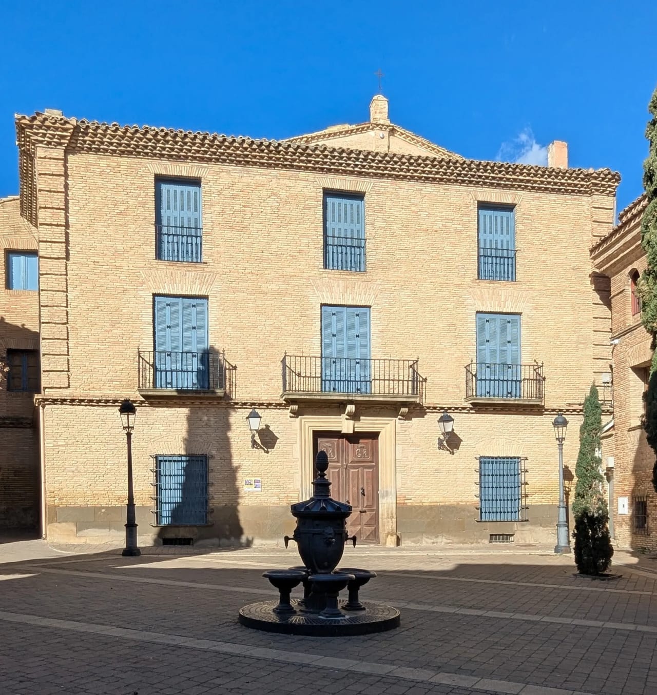 Edificio histórico con fachada de ladrillo y fuente en el centro de una plaza.