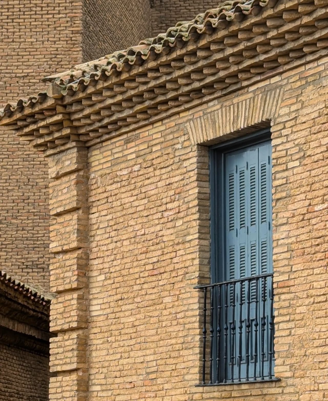Ventana con persianas azules y barandilla de hierro en edificio de ladrillo.